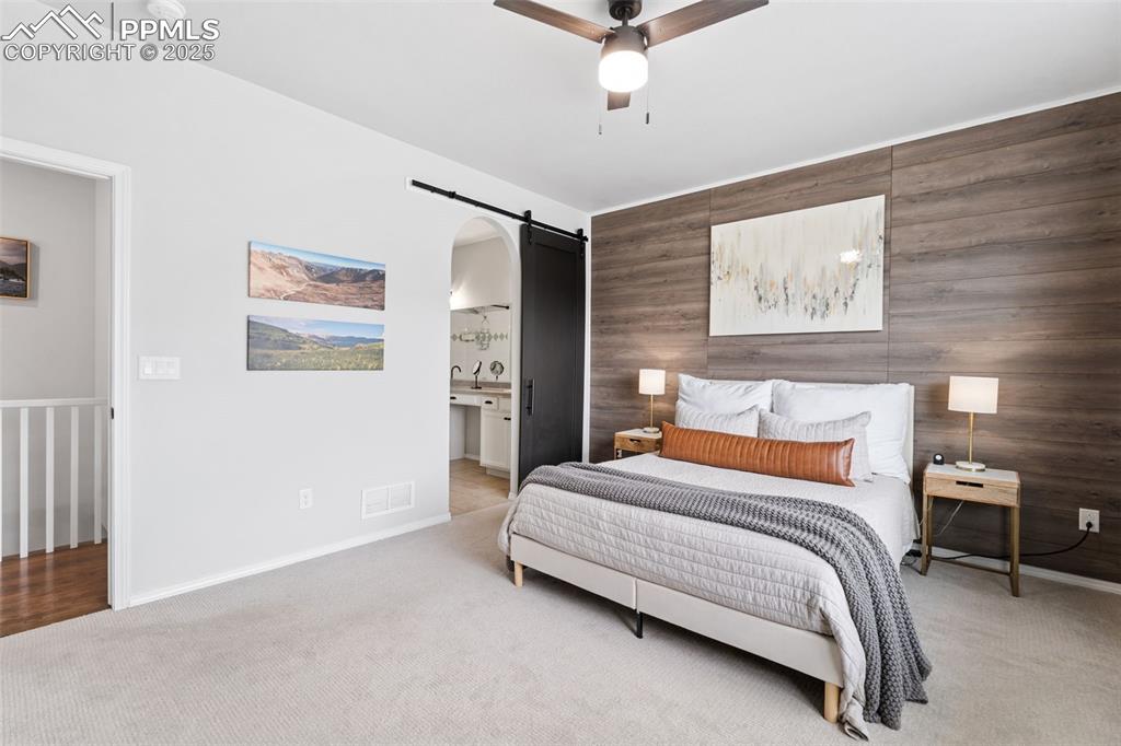 Image 11 of 22: Bedroom featuring a barn door, light carpet, and ceiling fan