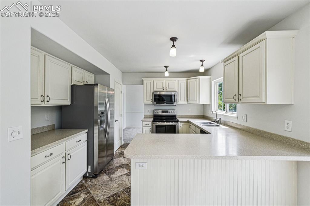 Image 10 of 46: Kitchen with appliances with stainless steel finishes, a peninsula, and lig
