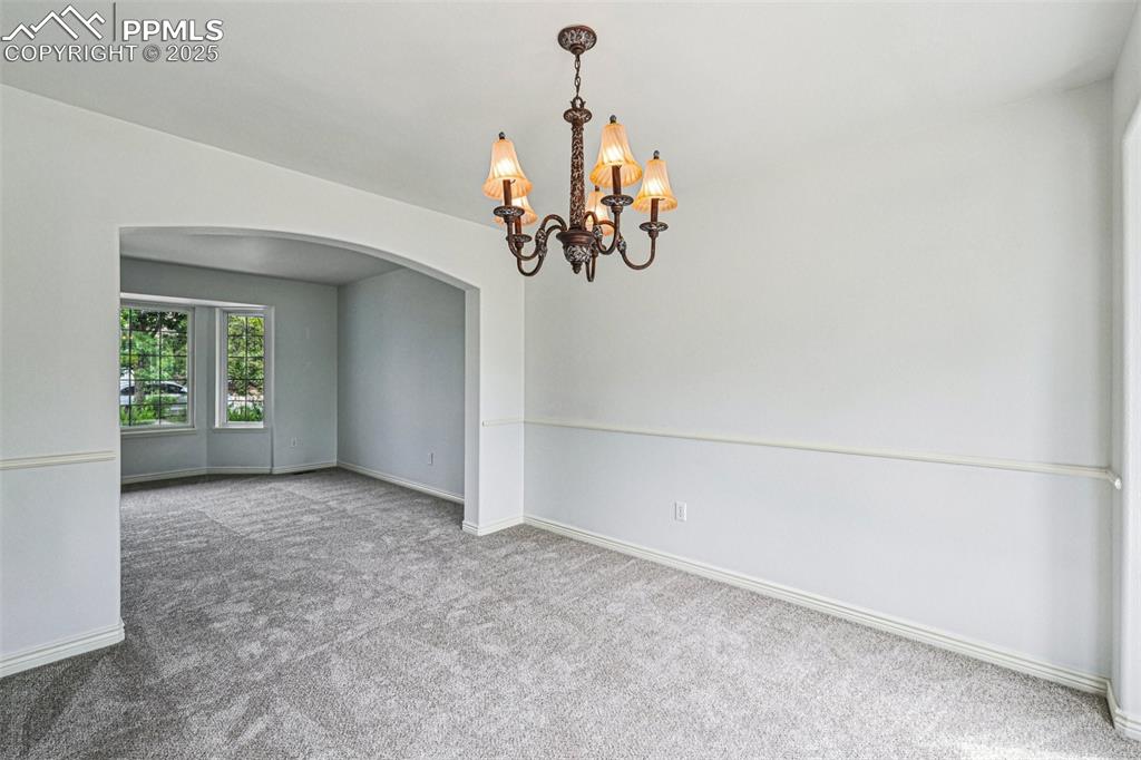 Image 12 of 46: Empty room featuring arched walkways, carpet, and a chandelier