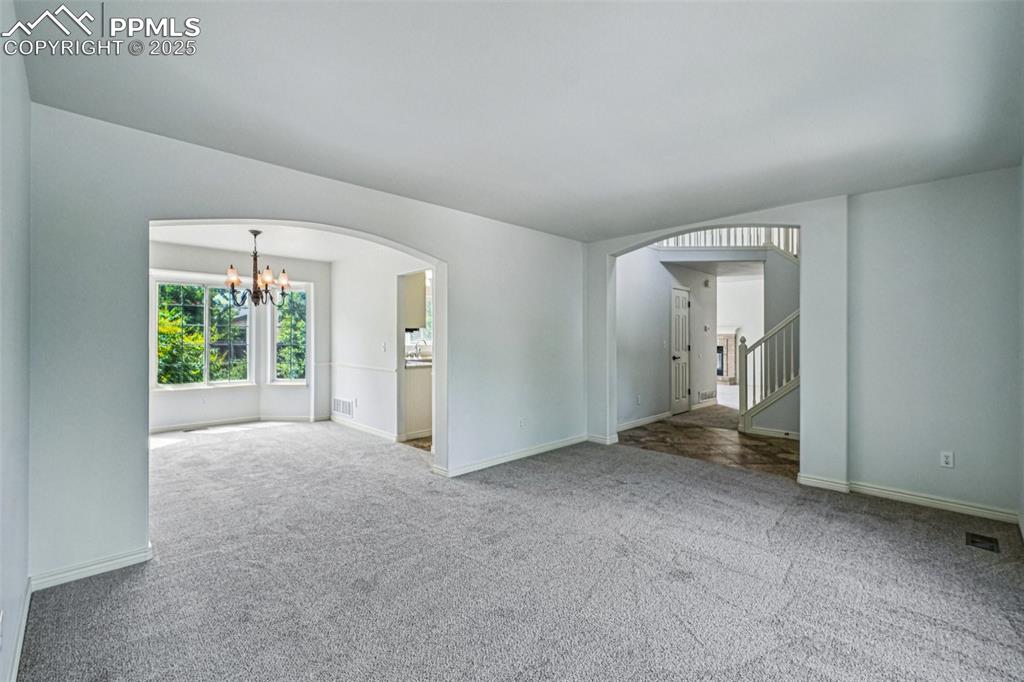 Image 13 of 46: Unfurnished room with arched walkways, a chandelier, carpet floors, and sta