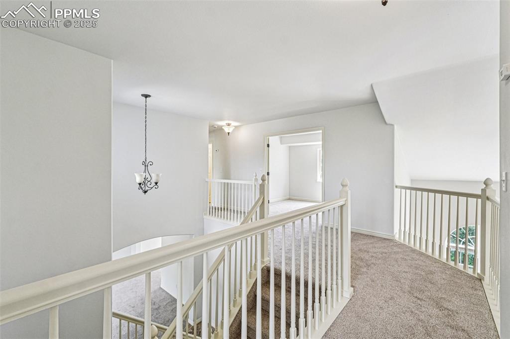 Image 18 of 46: Corridor with carpet flooring, an upstairs landing, and a chandelier