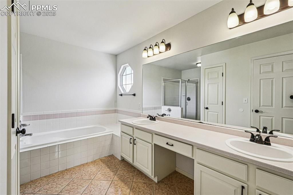 Image 22 of 46: Bathroom with double vanity, a stall shower, a bath, and tile patterned flo