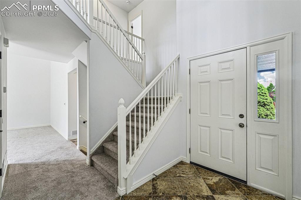 Image 4 of 46: Entryway with a towering ceiling, stairs, and dark colored carpet