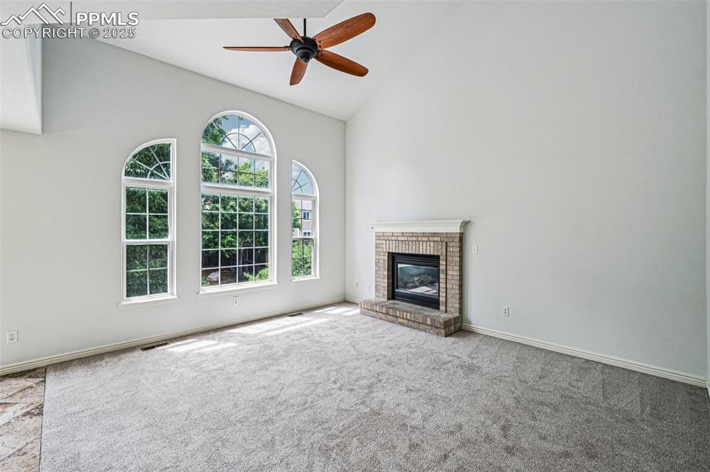 Image 5 of 46: Unfurnished living room featuring carpet, high vaulted ceiling, ceiling fan
