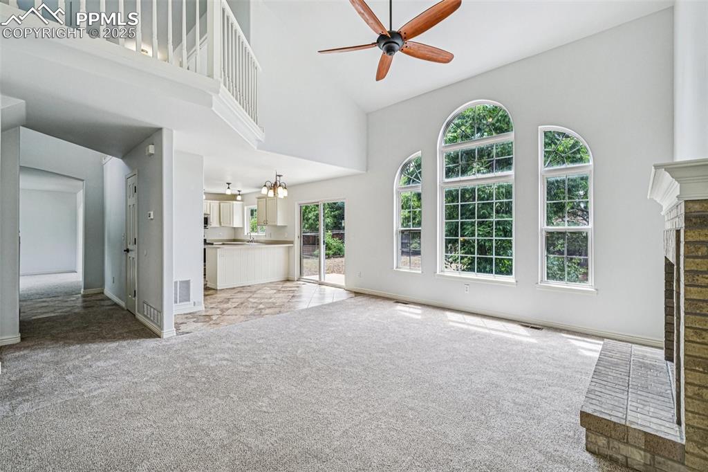 Image 6 of 46: Unfurnished living room with light colored carpet, a ceiling fan, a brick f