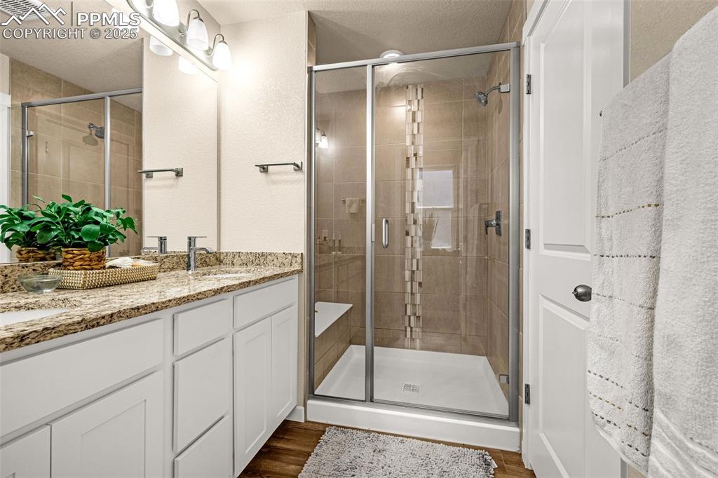 Image 14 of 35: Full bathroom with double vanity, a textured ceiling, a shower stall, and d