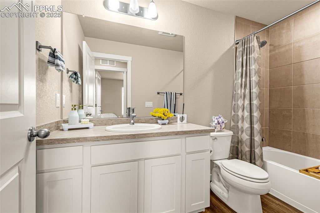 Image 19 of 35: Bathroom with a textured wall, shower / bath combo, vanity, and dark wood f
