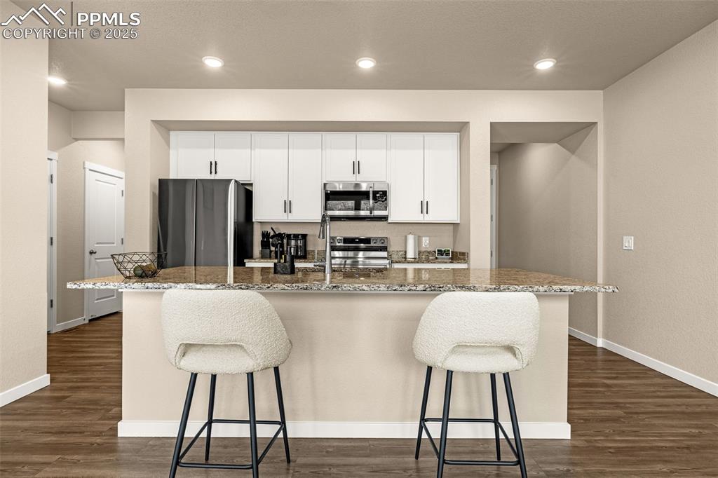 Image 6 of 35: Kitchen featuring white cabinetry, a breakfast bar area, light stone counte