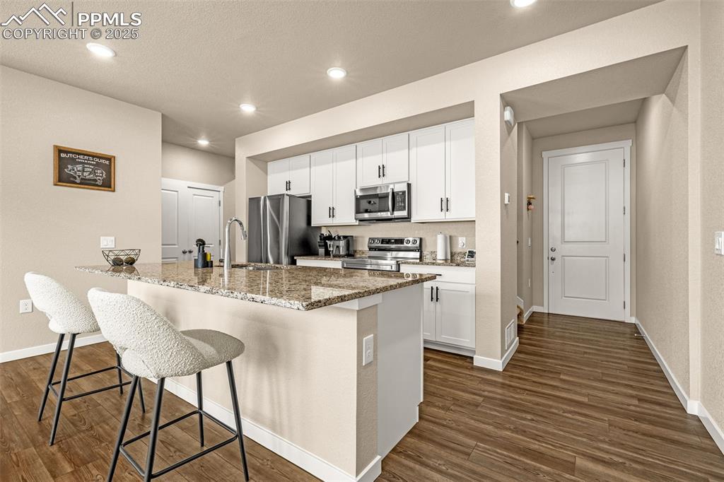 Image 7 of 35: Kitchen featuring light stone countertops, white cabinets, a kitchen breakf