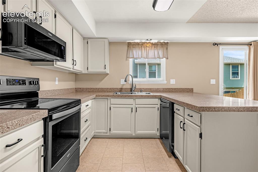 Image 10 of 32: Kitchen featuring white cabinetry, dark-finish appliances, light-toned coun
