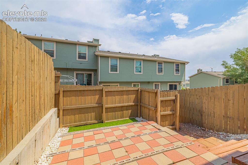 Image 22 of 32: Private fenced yard with a tiled patio and artificial turf