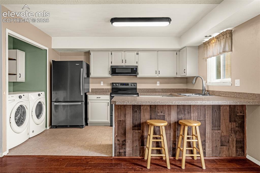 Image 8 of 32: Kitchen with light-colored cabinetry, dark appliances, and a wood-finish br