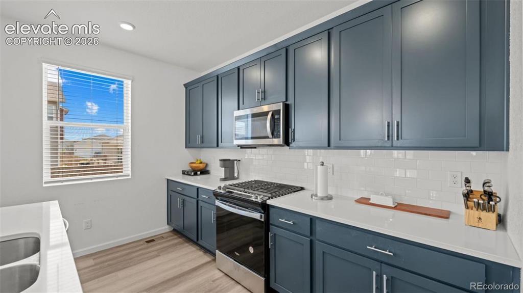 Image 10 of 38: Modern kitchen featuring blue cabinetry, stainless steel appliances, a whit