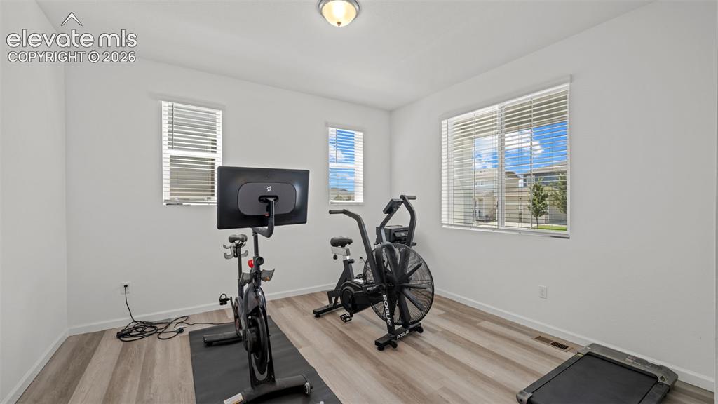 Image 5 of 37: Spacious room featuring wood-finish flooring, multiple windows with blinds,