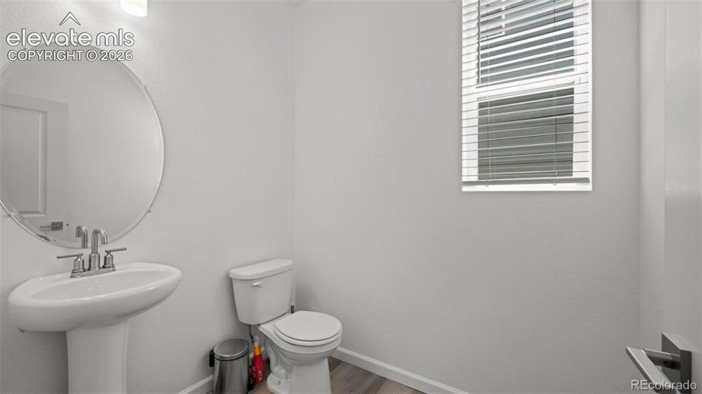 Image 6 of 38: Pedestal sink with chrome fixtures, circular mirror, and wood-finish floori