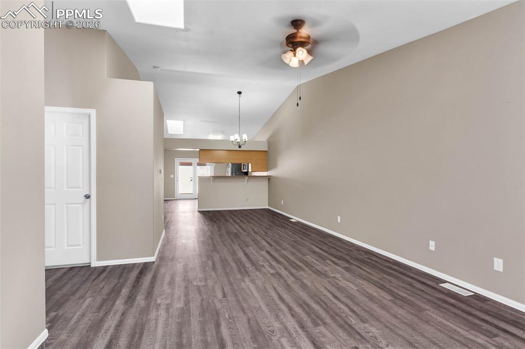 Image 4 of 28: Unfurnished living room featuring a skylight, dark wood-style floors, vault