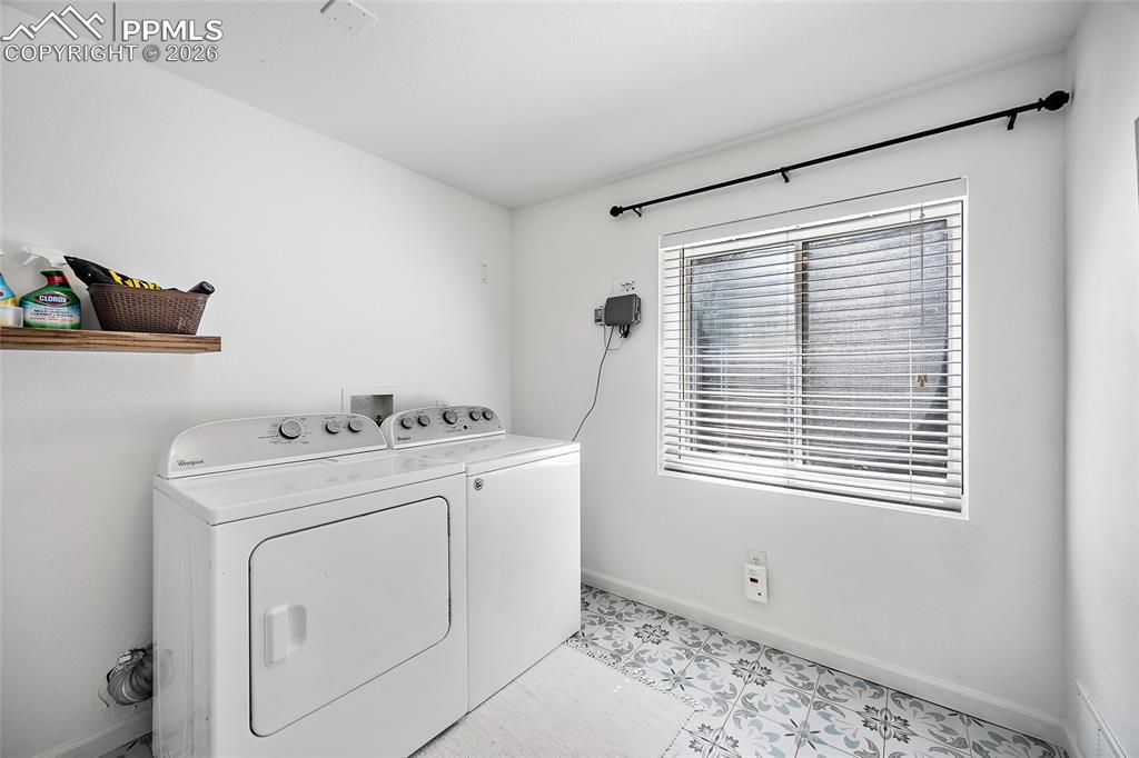 Image 27 of 46: Laundry area featuring a window with blinds, white walls, and decorative fl