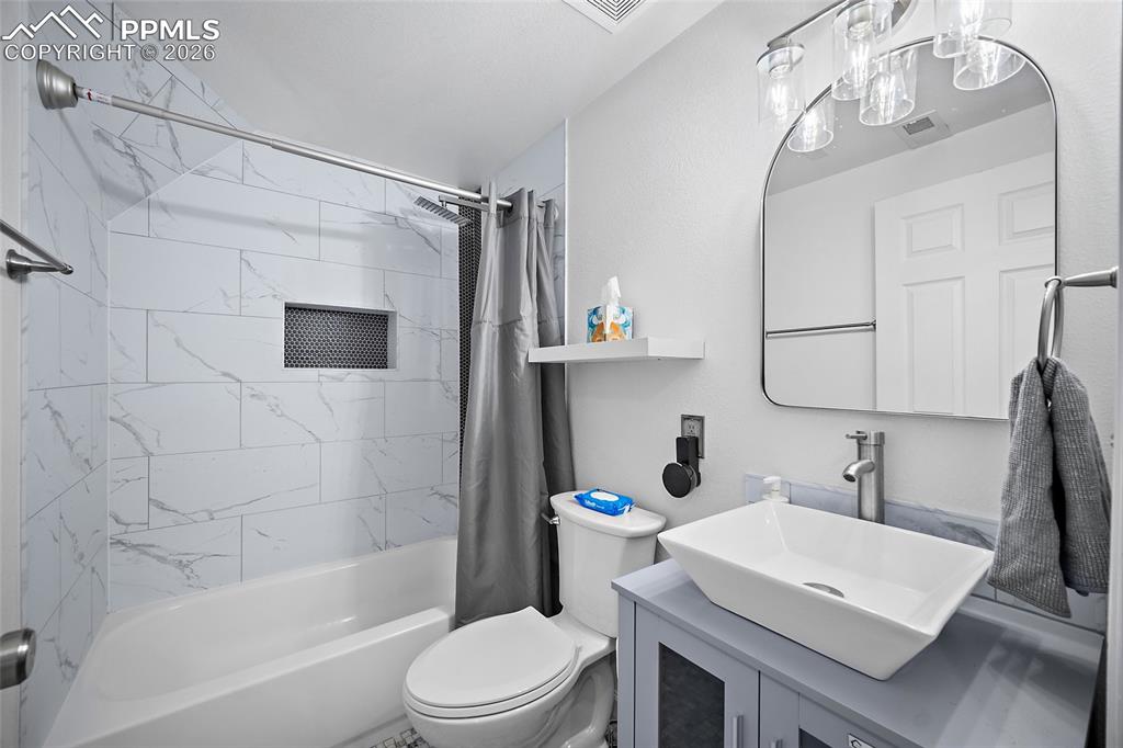 Image 33 of 46: Bathroom featuring a combination tub/shower with marble-patterned tile surr
