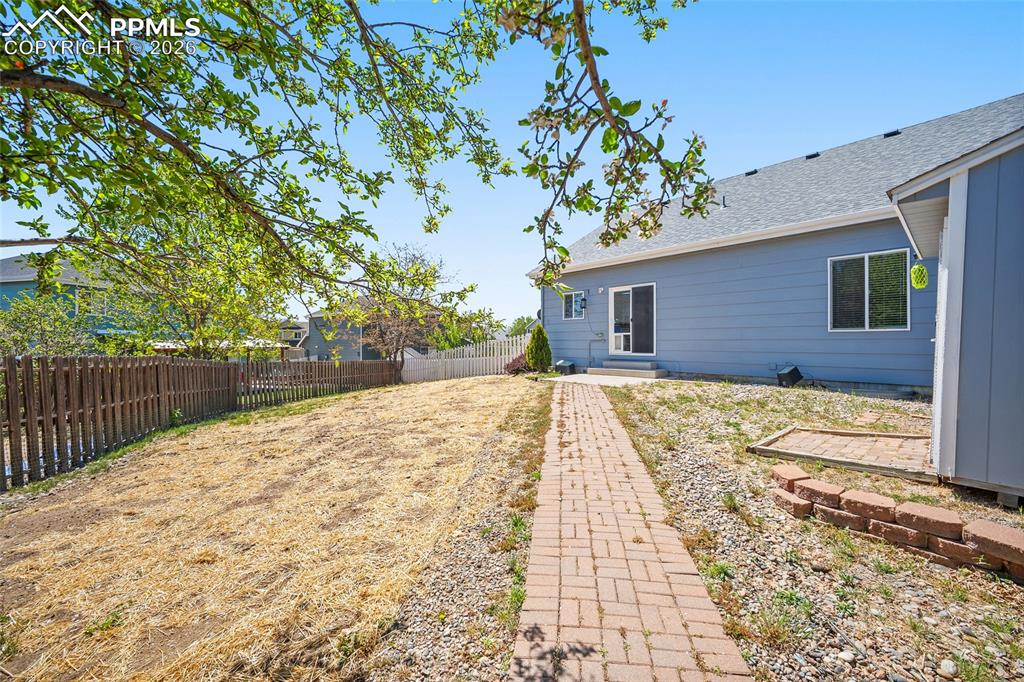Image 40 of 46: Spacious backyard featuring a brick paver pathway, privacy fencing, and a b