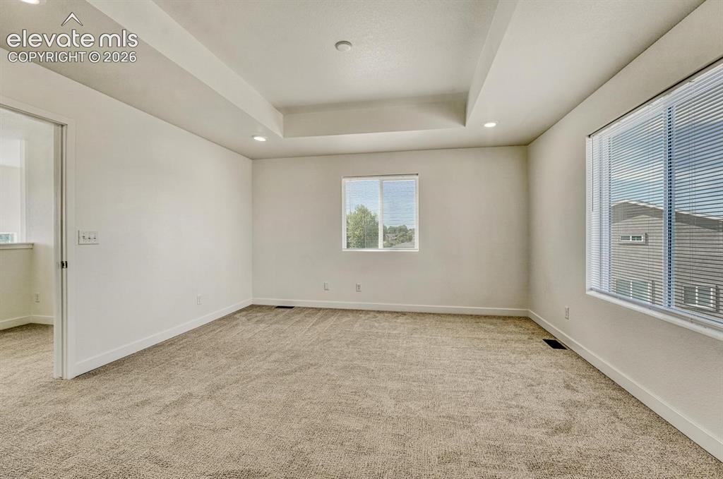Image 18 of 50: Primary bedroom features tray ceiling