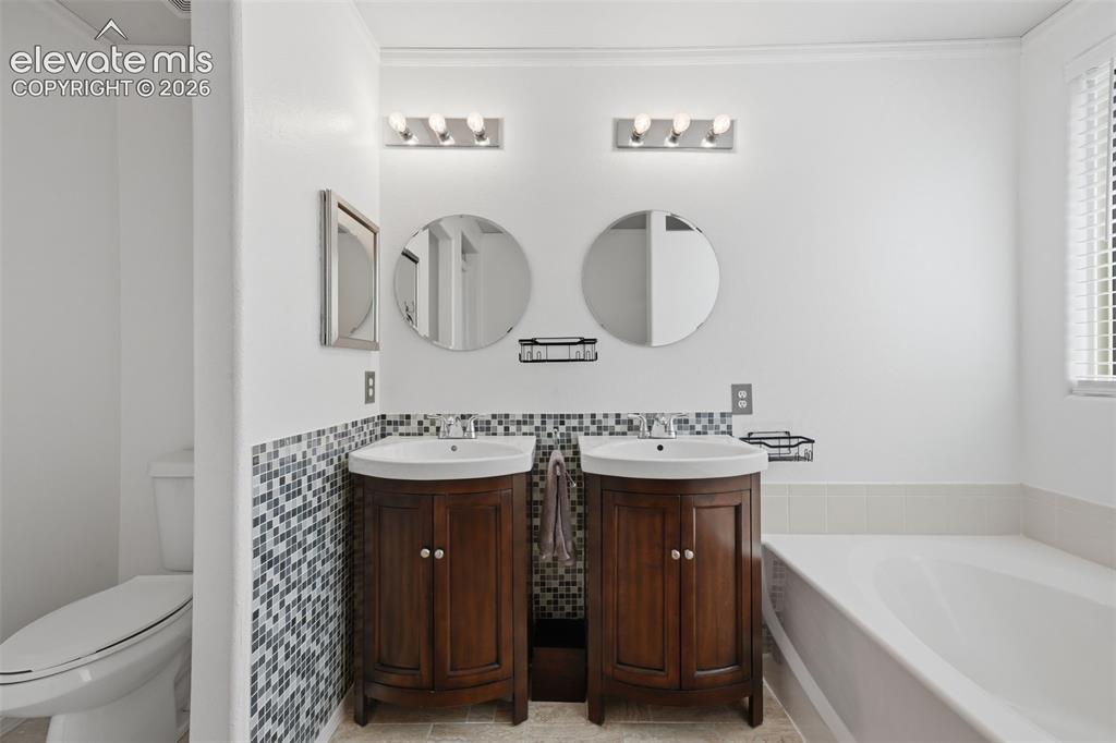 Image 23 of 35: Dual vanities with wood-finish cabinetry, mosaic tile wainscoting, and indi