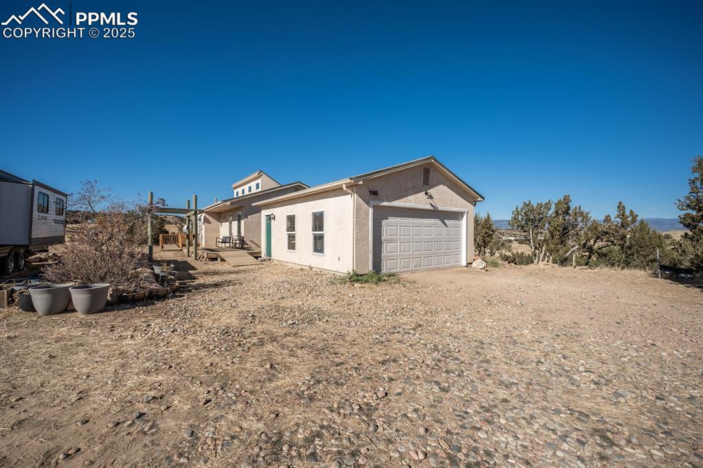 Image 33 of 50: View of side of property with stucco siding, dirt driveway, and a patio
