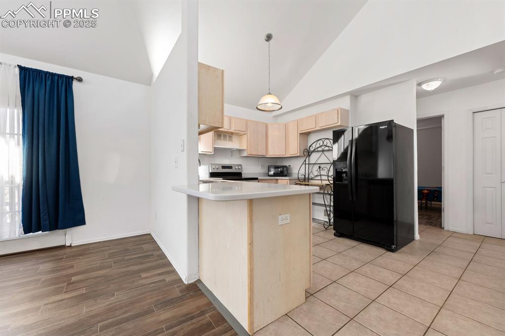 Image 39 of 50: Kitchen with light brown cabinets, black fridge with ice dispenser, high va