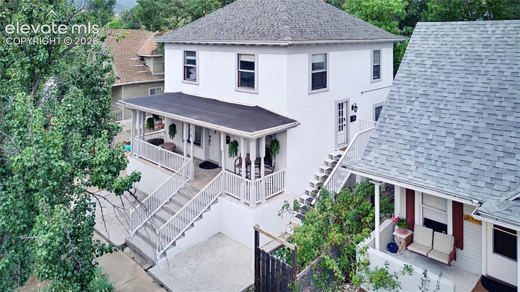 Caption: White exterior with multiple entry points, featuring a covered porch with railing and a shingle roof