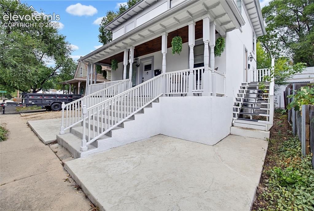 Image 2 of 50: White exterior with a covered porch, white railing, and dual entry staircas