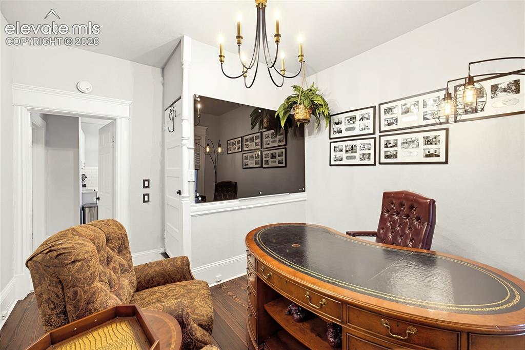Image 22 of 50: Hardwood flooring, cased doorway, overhead chandelier, wall-mounted light f
