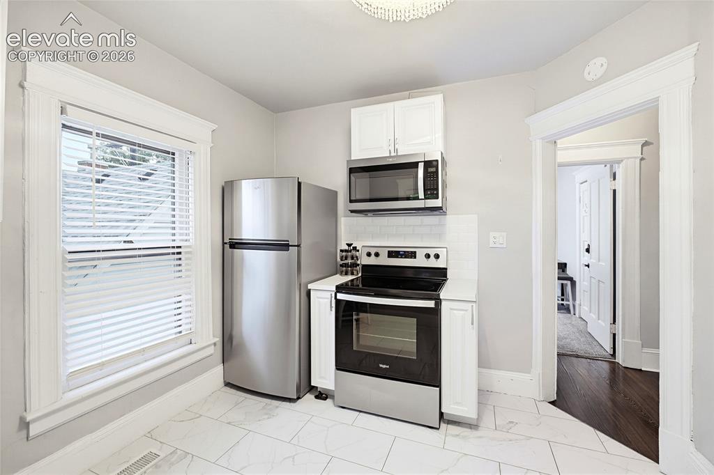 Image 36 of 50: Kitchen featuring stainless steel appliances, white cabinetry, a tiled back
