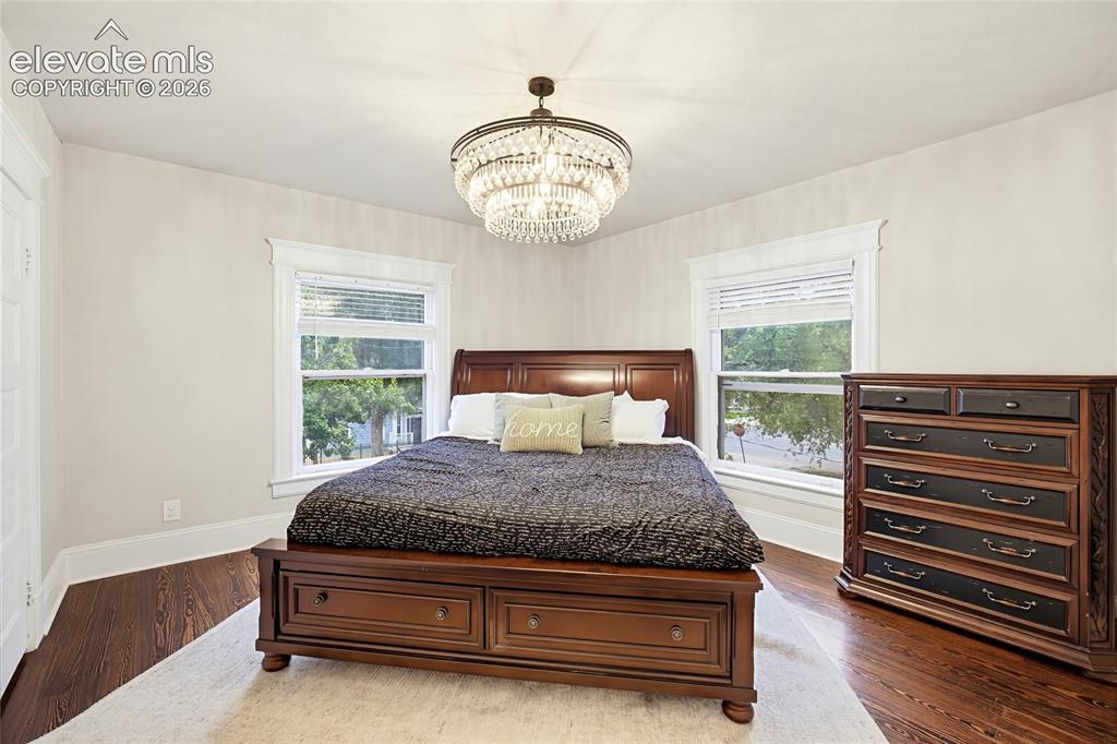 Image 37 of 50: Ornate chandelier, dark wood-finish flooring, white trim windows, and light