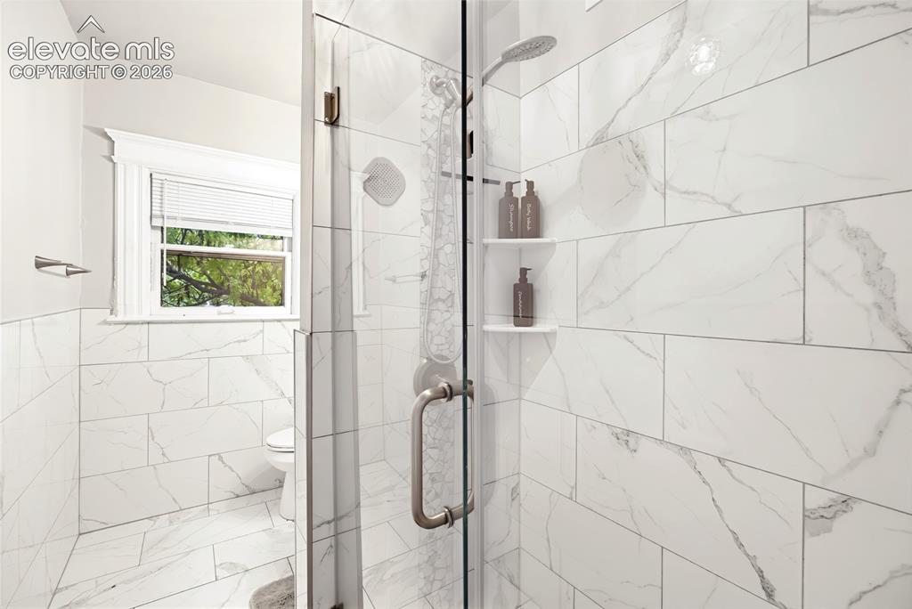 Image 41 of 50: Shower enclosure with glass door, white tile walls, and integrated shower s