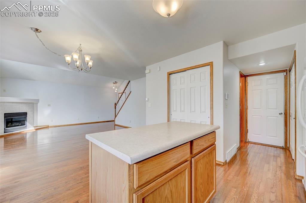 Image 10 of 34: Kitchen featuring light wood finished floors, a tiled fireplace, a chandeli