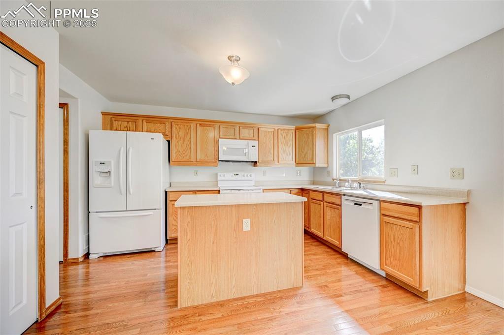 Image 8 of 34: Kitchen featuring white appliances, a center island, light countertops, lig