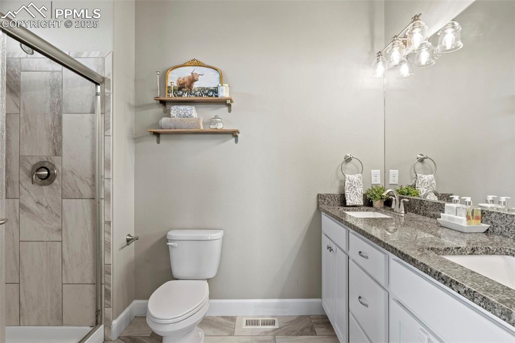 Image 27 of 30: Full bathroom featuring toilet, double vanity, a shower stall, and baseboar