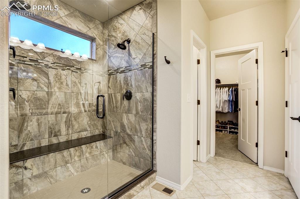 Image 30 of 48: Walk-in shower with full glass enclosure, built-in bench, and dual shower h
