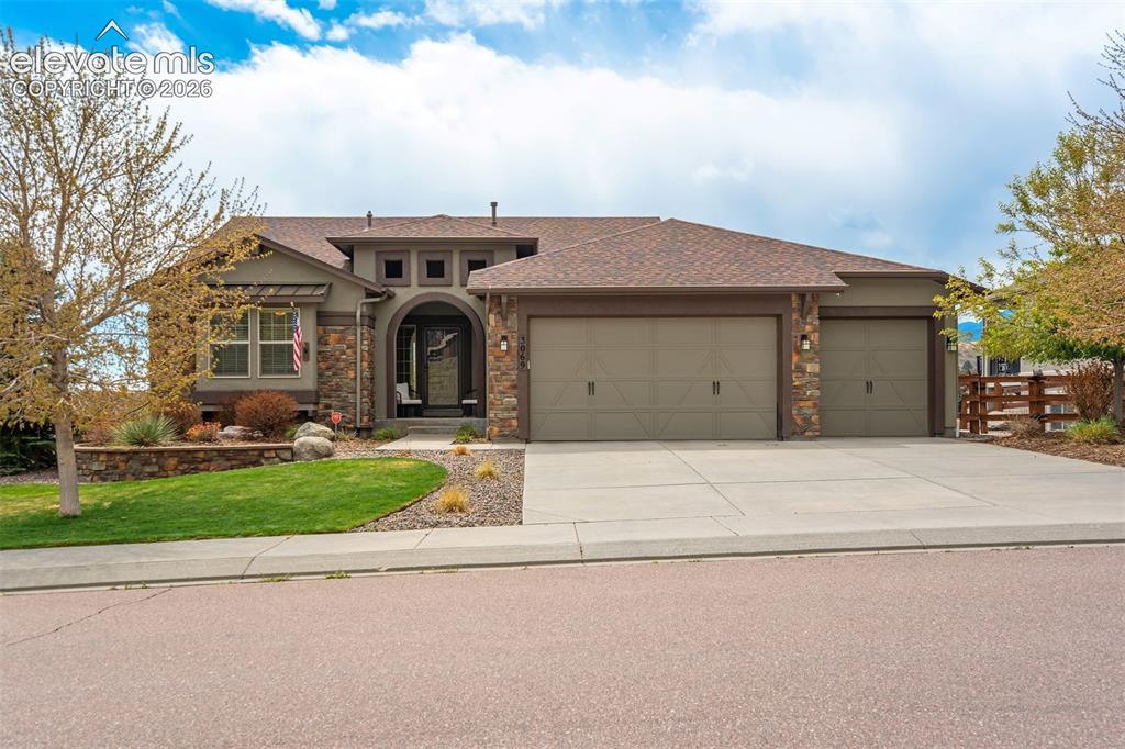 Image 4 of 48: Stucco and stone facade with a prominent arched entry, dual garage doors, a