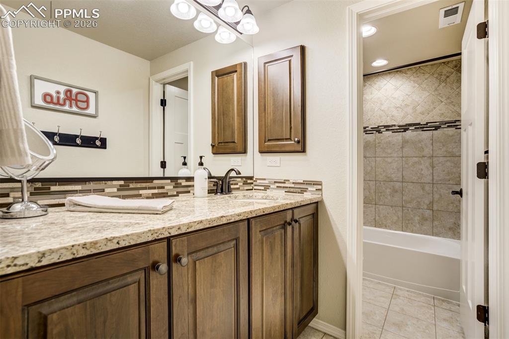 Image 44 of 48: Bathroom featuring a granite-look countertop, wood-finish cabinetry, a full