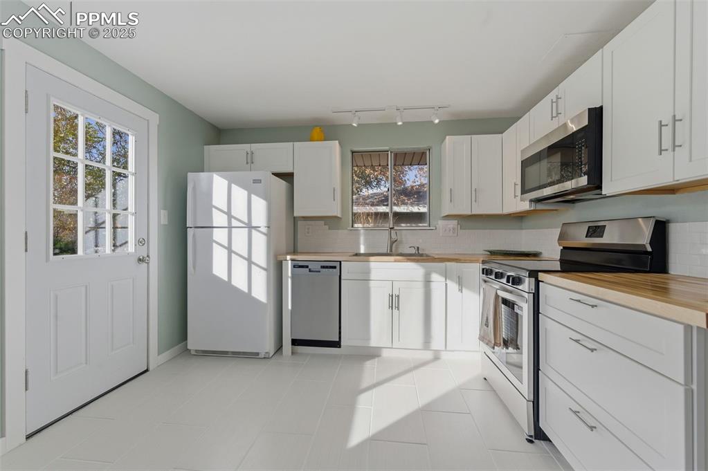 Image 8 of 38: Kitchen with stainless steel appliances, backsplash, white cabinets, and ce