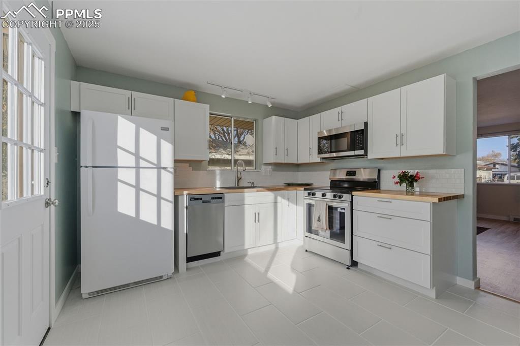 Image 9 of 38: Kitchen with stainless steel appliances, white cabinets, decorative backspl