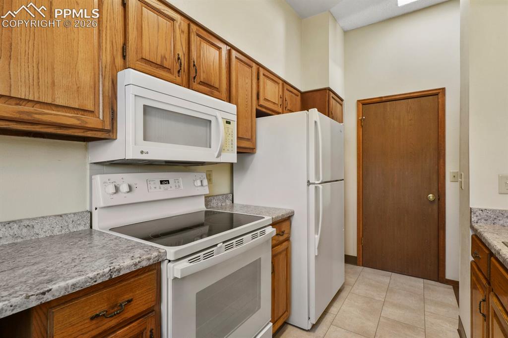 Image 15 of 27: Kitchen featuring wood cabinetry, light-toned countertops, white appliances