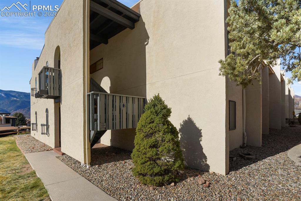 Image 3 of 27: Stucco exterior with a balcony and exterior staircase, surrounded by gravel