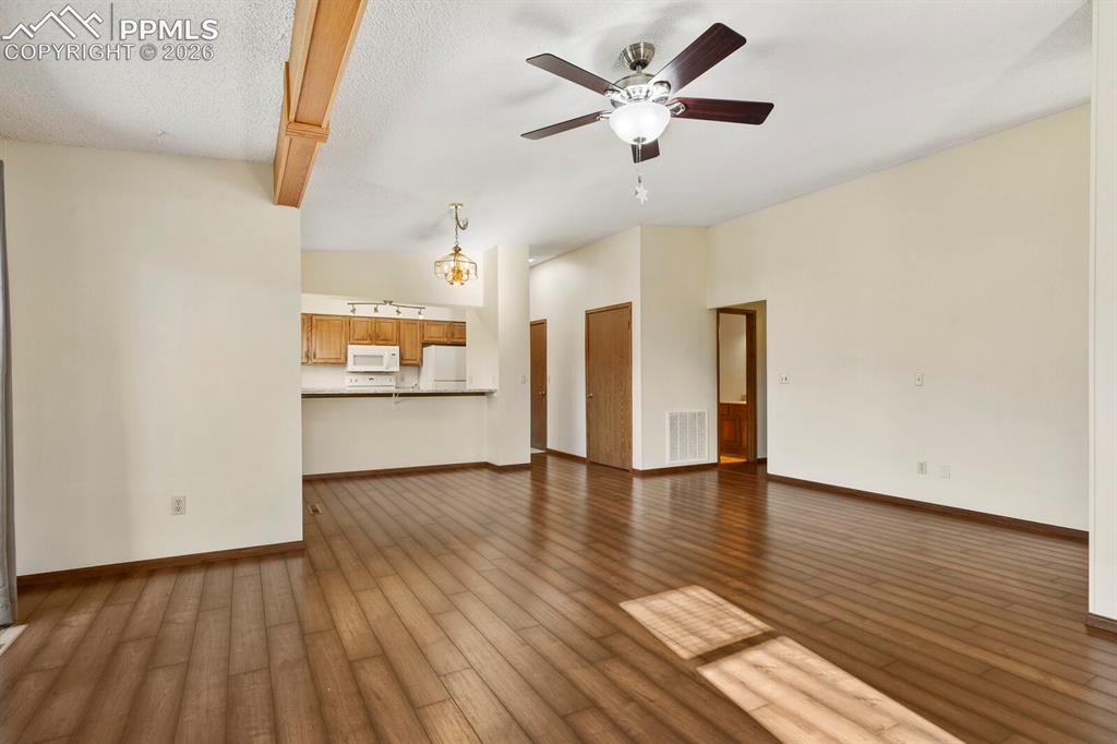 Image 8 of 27: Spacious living area featuring wood-finish flooring, a ceiling fan with int