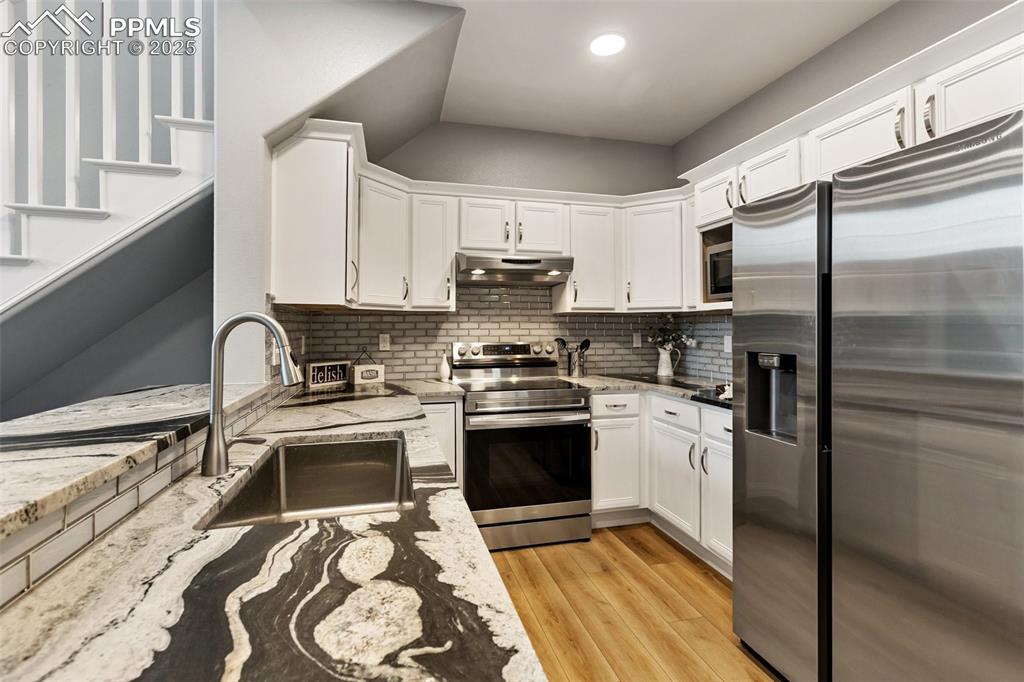 Image 16 of 44: Kitchen with stainless steel appliances, backsplash, white cabinetry, light