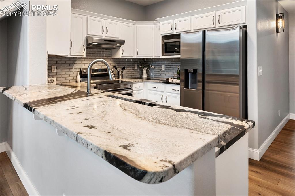 Image 17 of 44: Kitchen with dark wood-style flooring, light stone countertops, stainless s