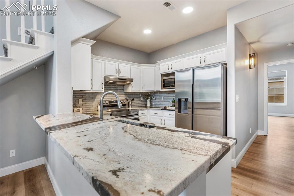 Image 18 of 44: Kitchen with white cabinets, light stone countertops, backsplash, appliance