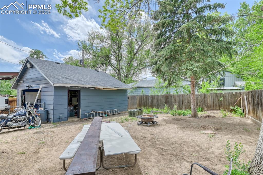 Image 7 of 37: Fenced backyard with a fire pit and an outdoor structure