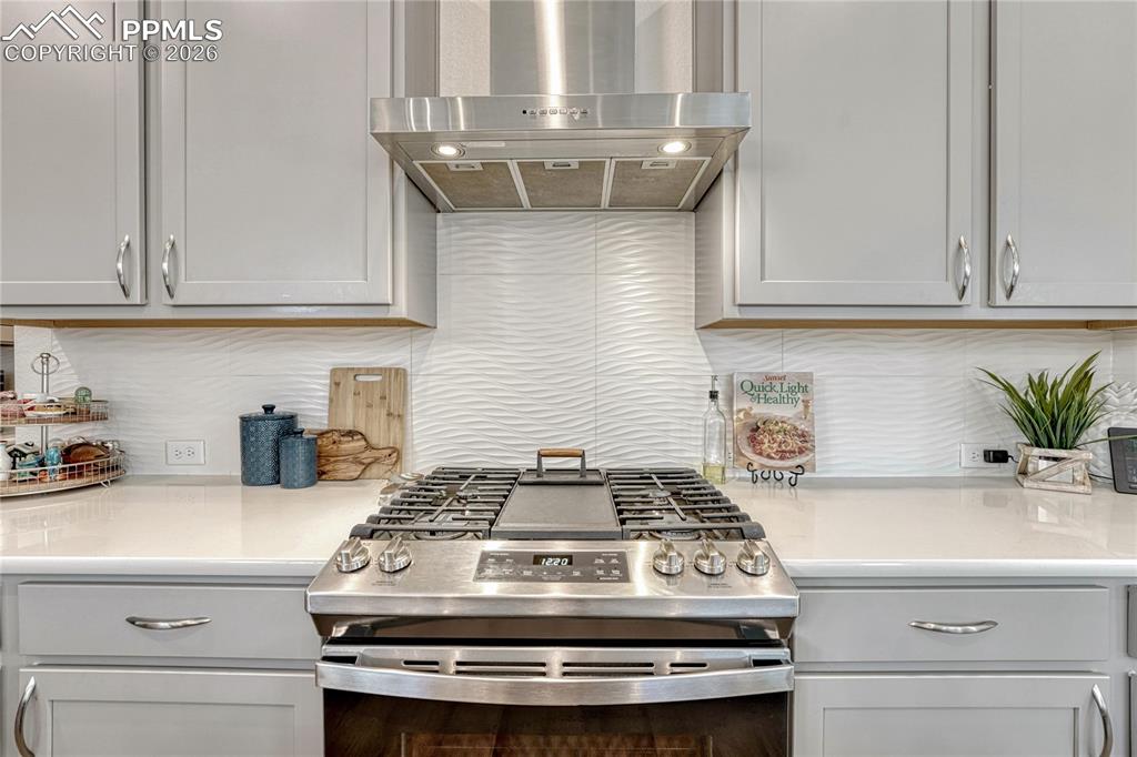 Image 14 of 50: Beautiful full height, white backsplash and a full gas range, center griddl
