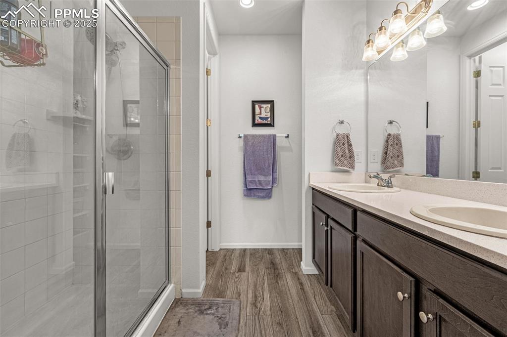 Image 25 of 37: Bathroom with double vanity, a stall shower, dark wood finished floors, and